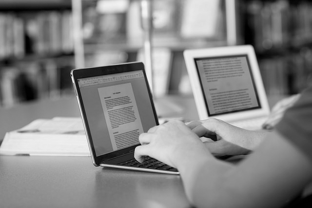 Writing a document on a laptop in the library - greyscale version