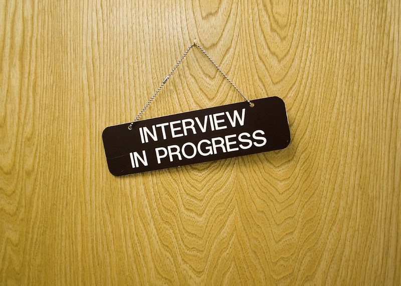 Image of closed door with "Interview in Progress" sign hanging on it