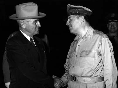 A picture of President Truman in a suit and hat shaking the hand of General Macarthur's. 
