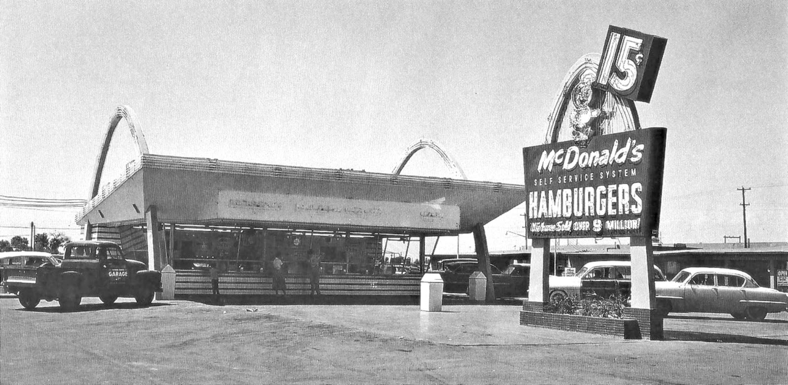 The McDonald's building is bookended by two giant arches. A large free-standing sing in front of the building read "15 cents; McDonald's self service system Hamburgers; welcome sold over 9 million." The sign has only a single arch. 