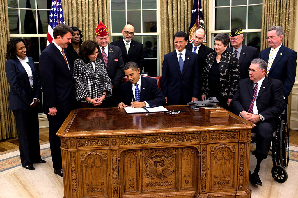 President Obama signing an executive order in the Oval Office with a number of witnesses standing behind him.