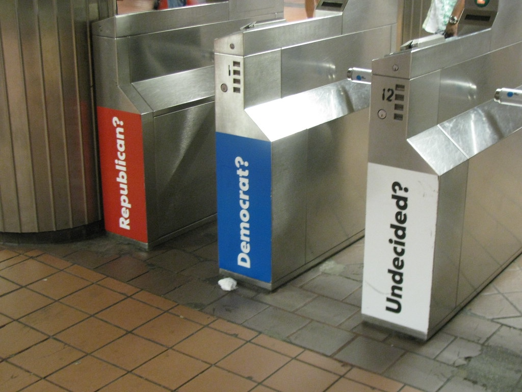 Three public train station turnstiles with "Republican?" "Democrat?" and "Undecided?" signs on them.