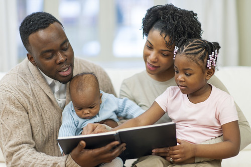 A father and mother with their two young children, reading a book together.