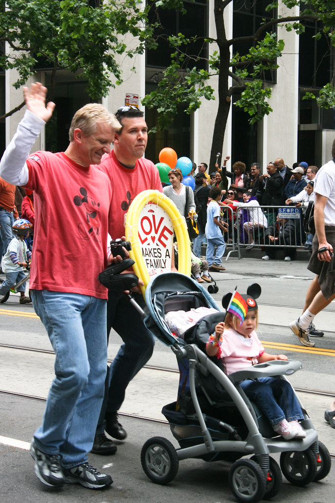 A gay couple walking during a pride parade with their young daughter in a stroller.