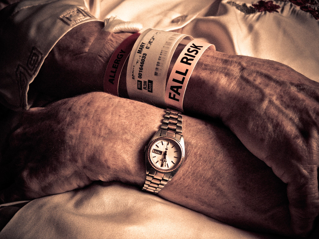 Older adults arms crossed with hospital bracelets on, including one that says, "Fall risk."