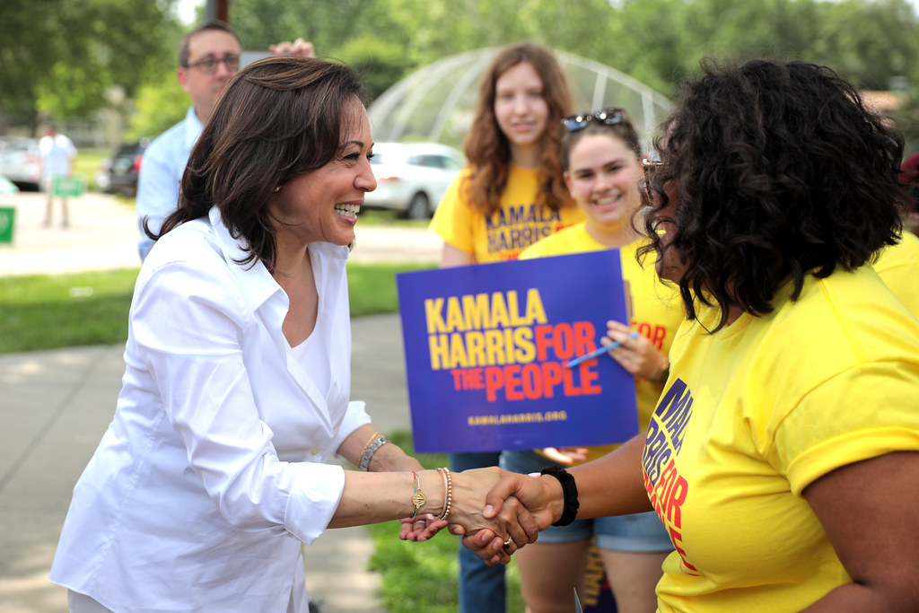 Kamala Harris shaking hands with a supporter during her campaign, with other supporters in the background.