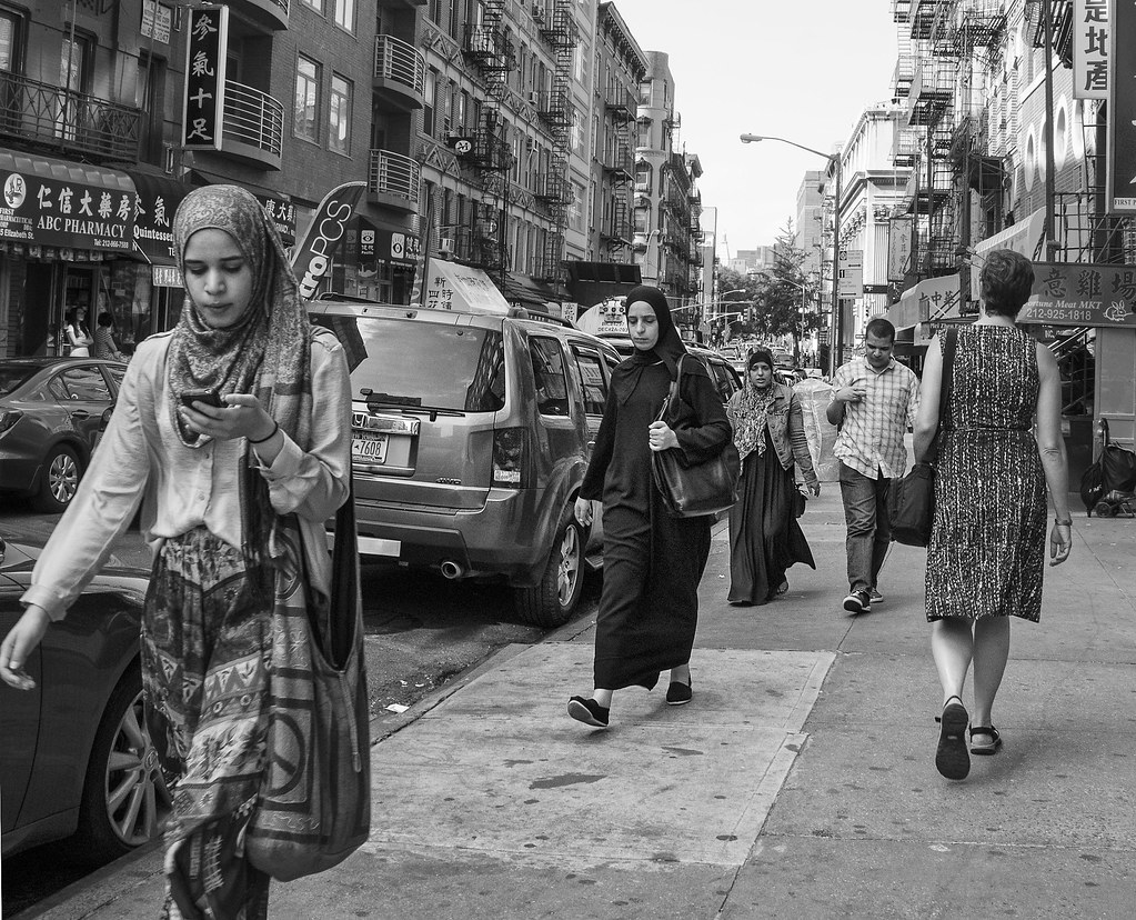 Busy New York street with three women with hijabs walking up the sidewalk.