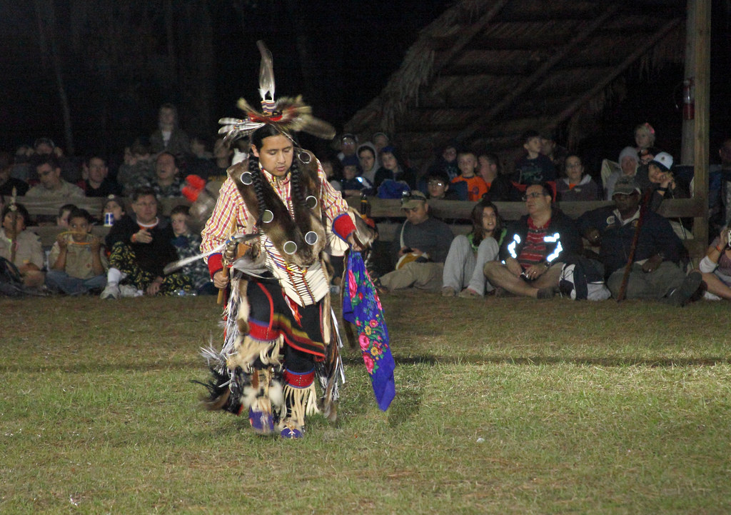 American Indian dancing in traditional dress at a modern day Pow Wow in front of guests.