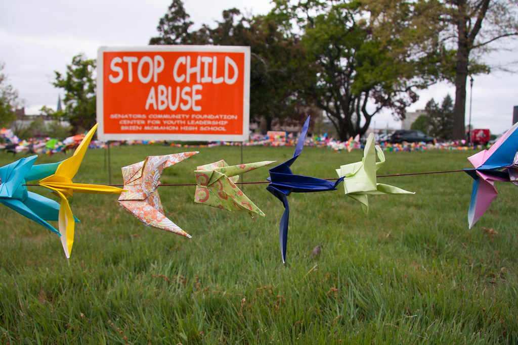 Origami cranes on a line with a billboard in the background that says "Stop Child Abuse."