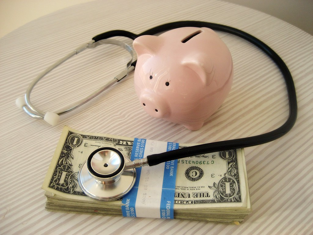 A stethoscope on money and surrounding a piggy bank.