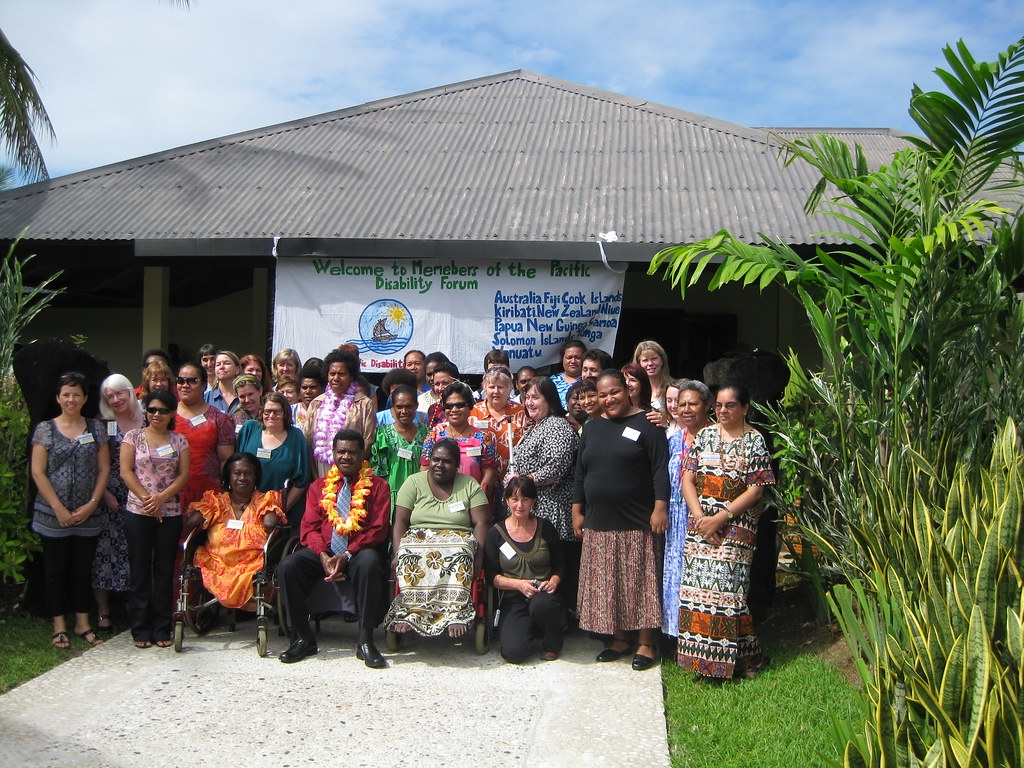Group of people posing for a picture in front of a banner that says, "Welcome to Members of the Pacific Disability Forum.
