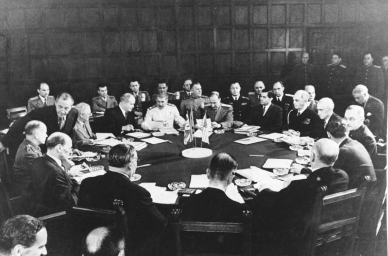 A black and white picture of a Potsdam Conference session which includes many men sitting around a large table. Included in the group are Clement Attlee, Ernest Bevin, Vyacheslav Mikhailovich Molotov, Joseph Stalin, William D. Leahy, Joseph E. Davies, James F. Byrnes, and Harry S. Truman. 