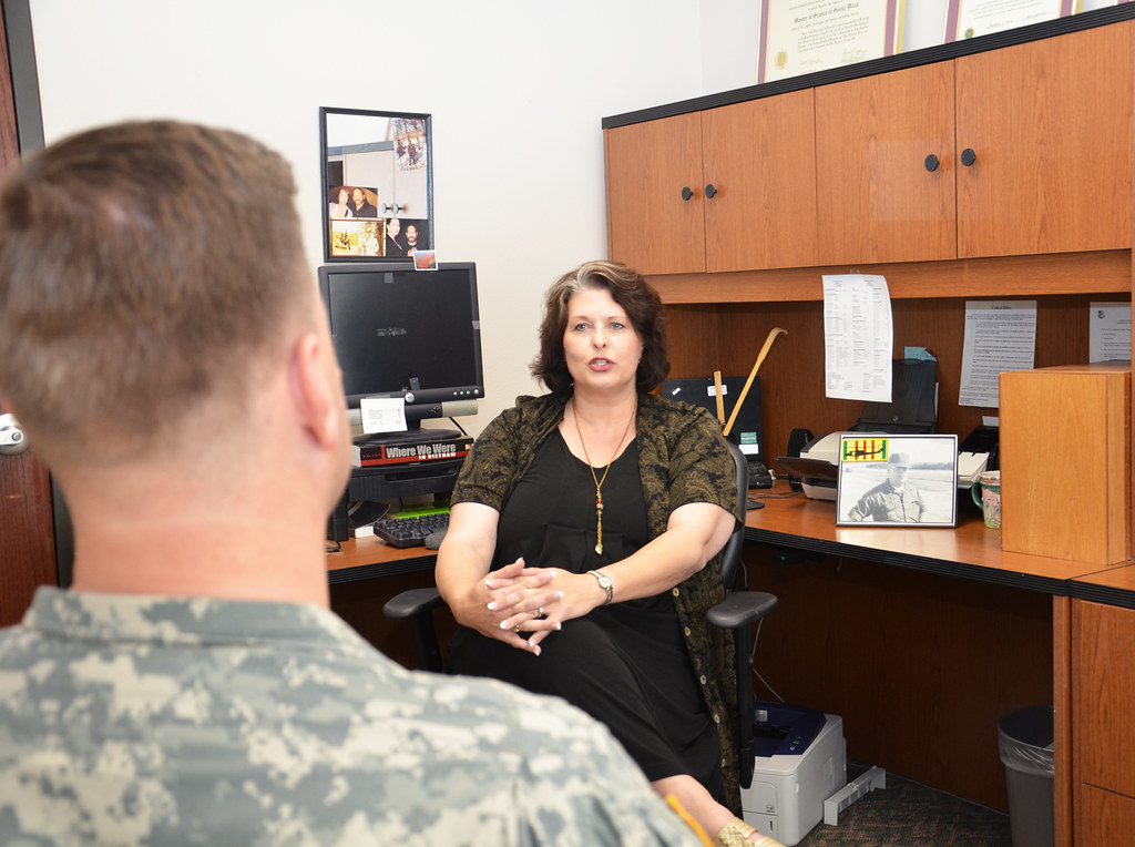 Social worker in the background facing the camera and talking with a client who is a veteran in the foreground.
