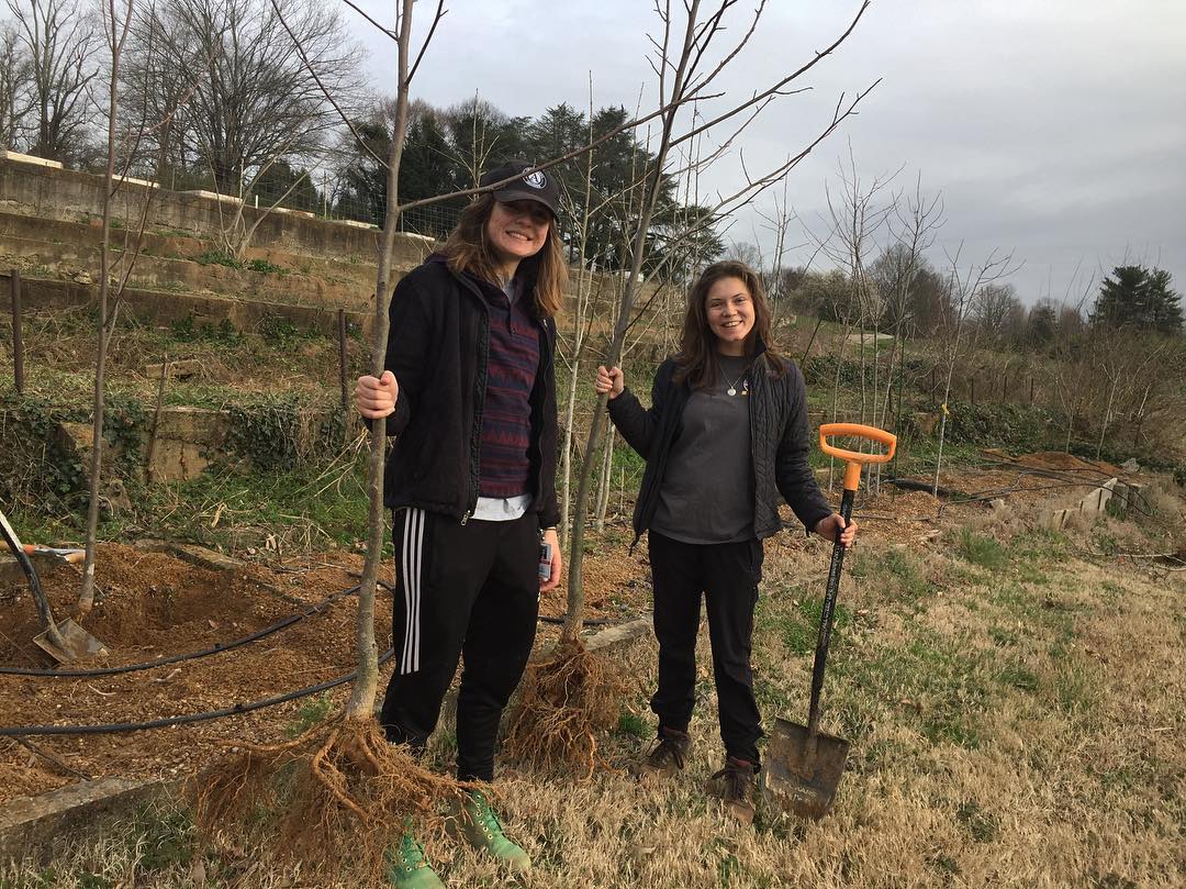 Two women hold up bare root trees that have been harvested from a Missouri Gravel Bed system