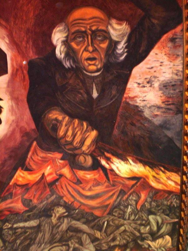 The expressionistic painting depicts Miguel Hidalgo y Costilla holding his left hand above his head and his right hand waving a red flag. He stands atop a group of men also waving red flags.
