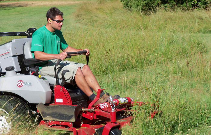 A person on a red riding mower drives through tall grass