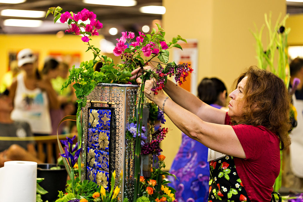 A person works on a large, elaborate flower arrangement at a trade show or similar event