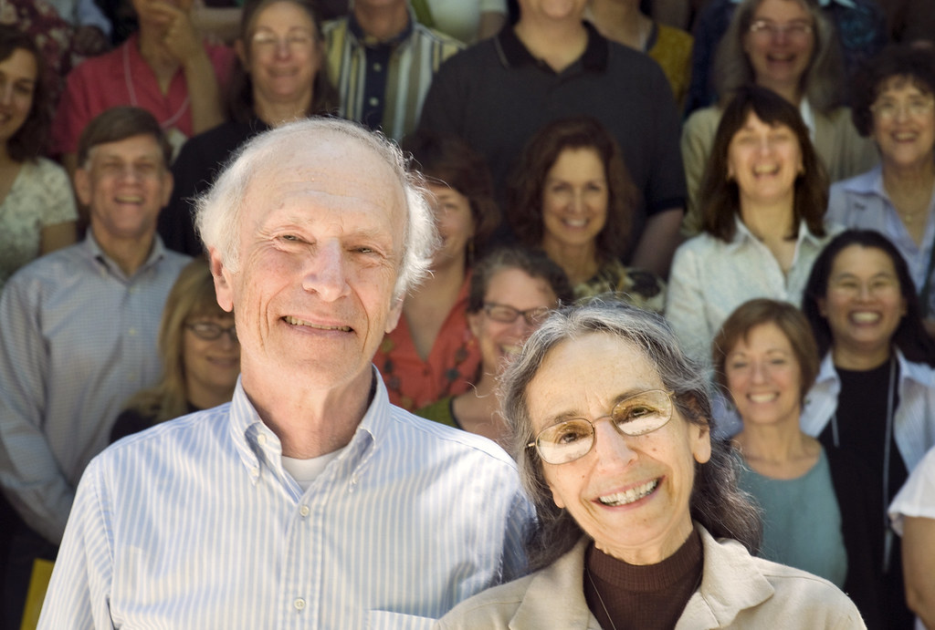 A smiling man and woman stand in front of a crowd of smiling people.