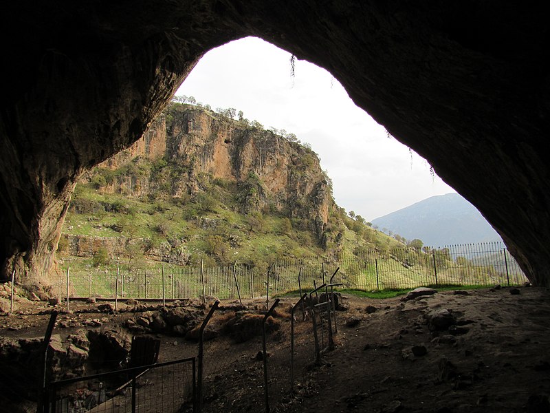 A view of an archaeological site from the mouth of a cave.  A mountain is beyond the entrance.