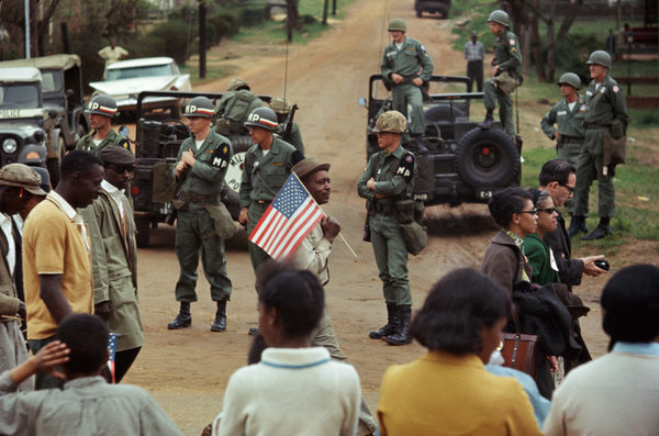  Man with American flag and marchers walking past federal troops guarding crossroads, 1965.