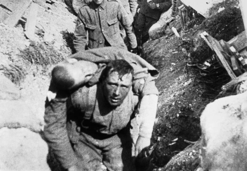 photo of man looking at camera while carrying a corpse on his back through the trench
