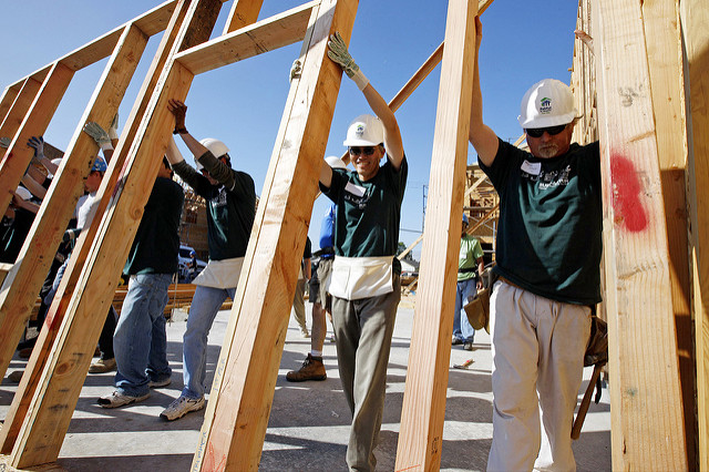 Photo of Habitat for Humanity team of people lifting a framed wall of a house. 